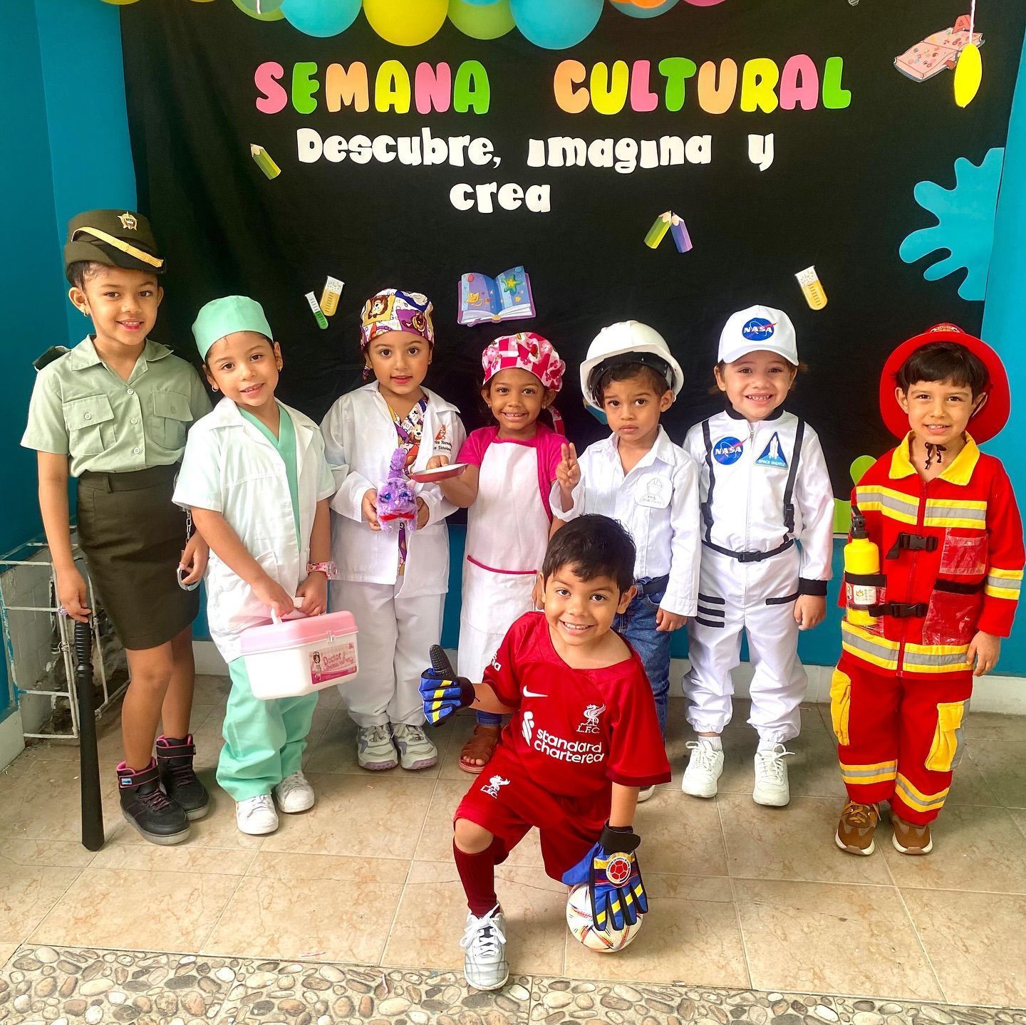 Un grupo de estudiantes reunidos alrededor de una mesa; algunos parecen estar dando clase. Al aire libre, soleado.
