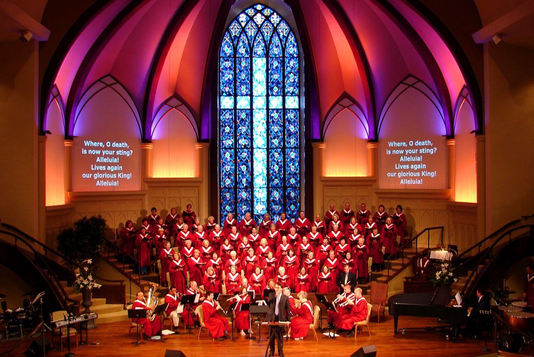 A choir is performing in front of a large stained glass window