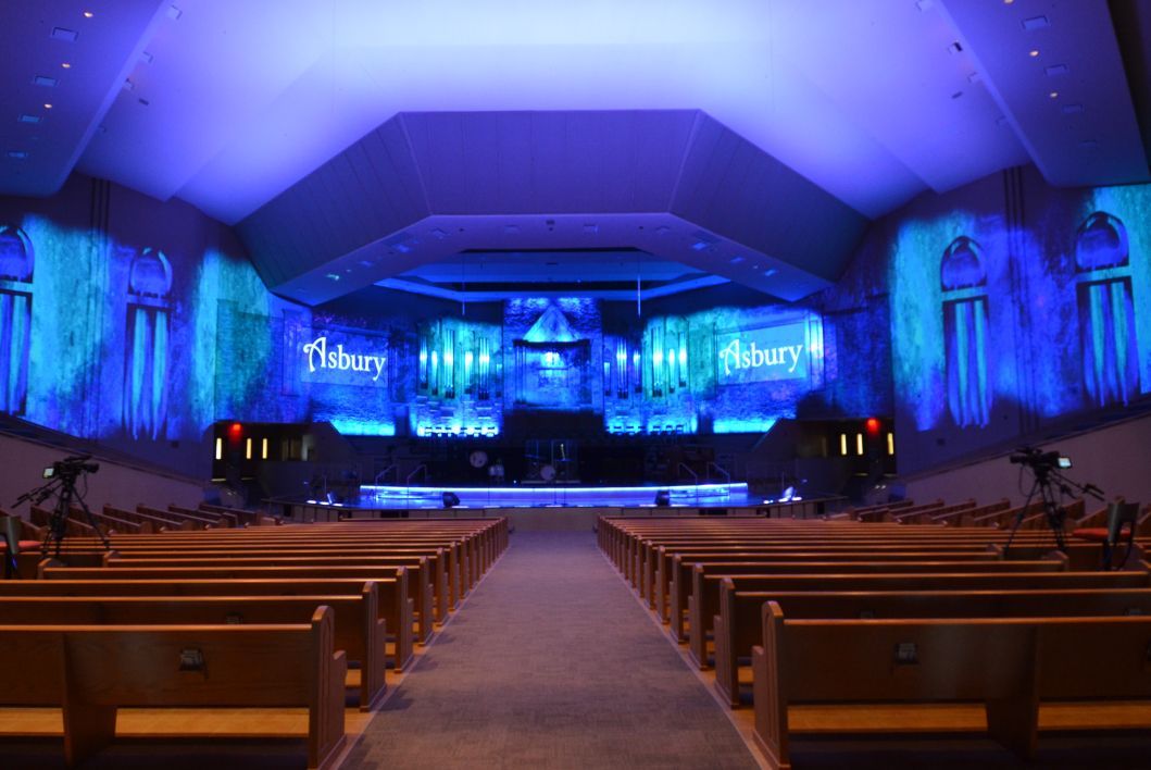 A church with rows of wooden benches and a stage with blue lights projected on the walls.