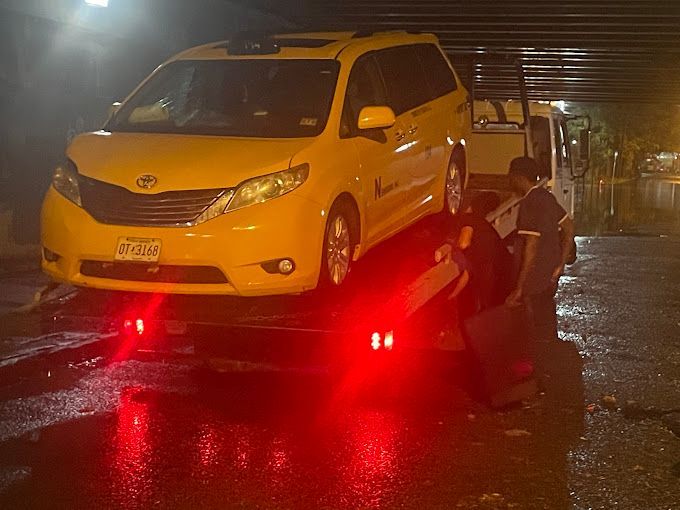 A yellow minivan is being towed by a tow truck at night.