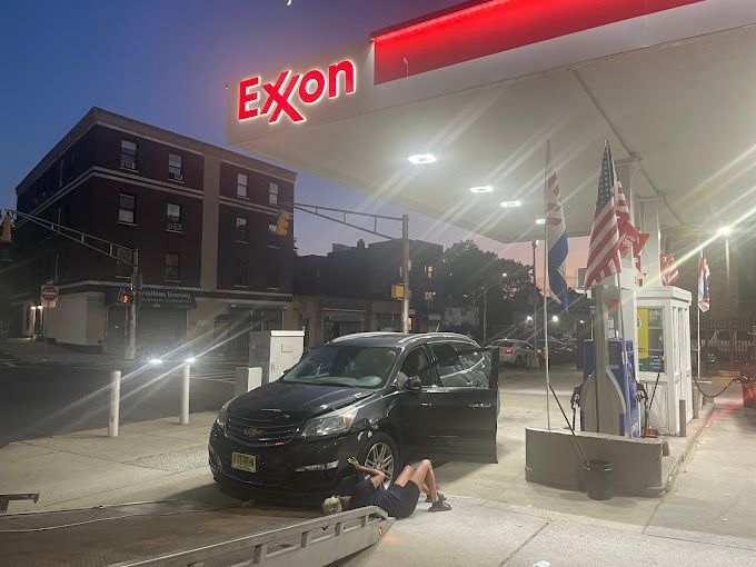 A man is laying on the ground next to a car at a gas station.