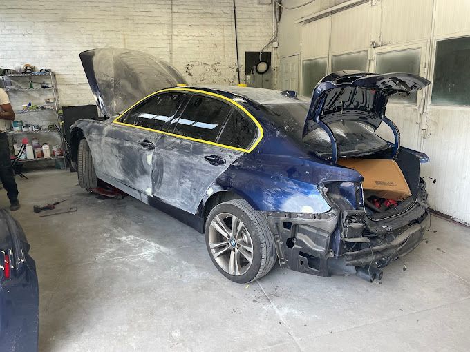 A blue car is sitting in a garage with the hood open.