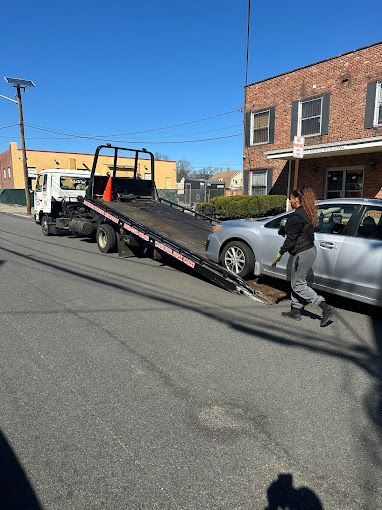 A tow truck is towing a silver car down the street.