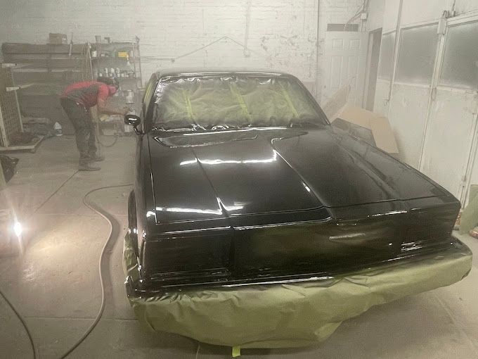 A black car is being painted in a garage.