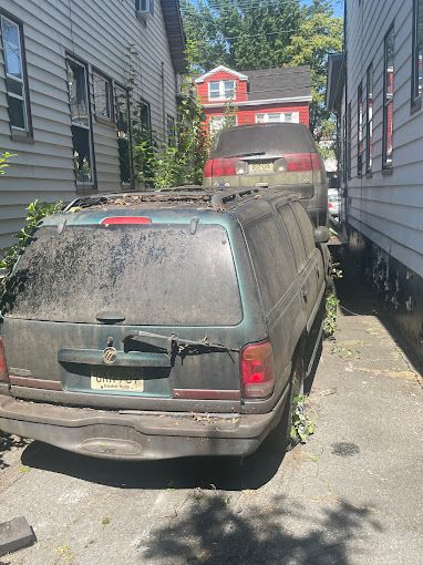 A dirty suv is parked in a parking lot between two houses.