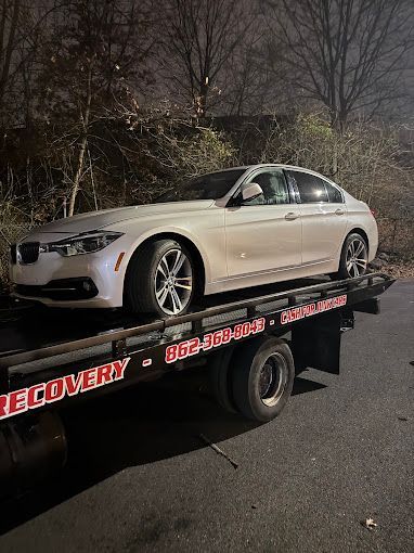 White BMW sedan on a tow truck at night, with a Recovery company logo.