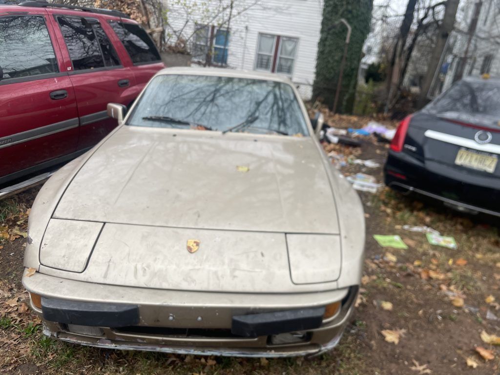 A dirty car is parked in a parking lot next to a red suv.
