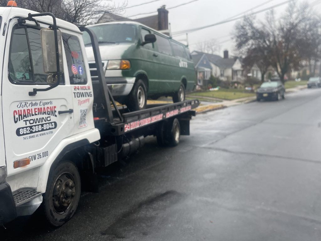 A tow truck is towing a green van down a street.