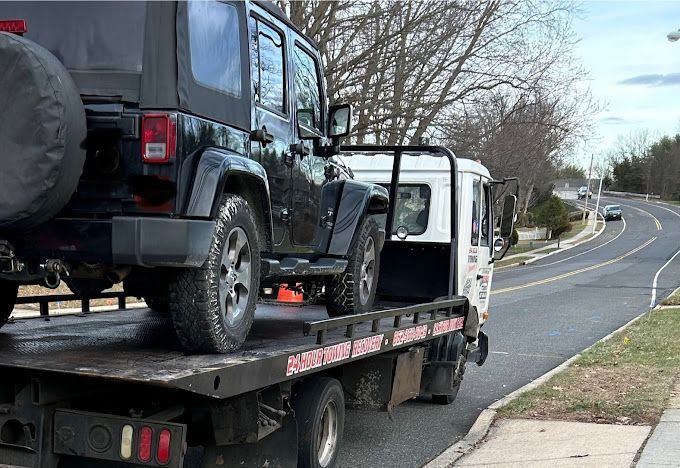 A black jeep is being towed by a tow truck.
