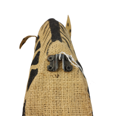 Een wanddecoratie van een opgezette giraffe, gemaakt van lichtbruin jute met zwarte stippen op een witte achtergrond.