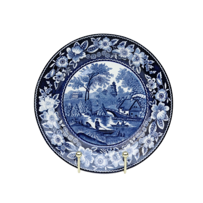 Blauw-wit porseleinen bord met een bloemenrand rondom een landschap met een gebouw, brug en beekje.