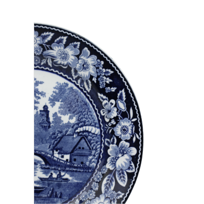 Blauw-wit porseleinen bord met een bloemenrand rondom een landschap met een gebouw, brug en beekje.