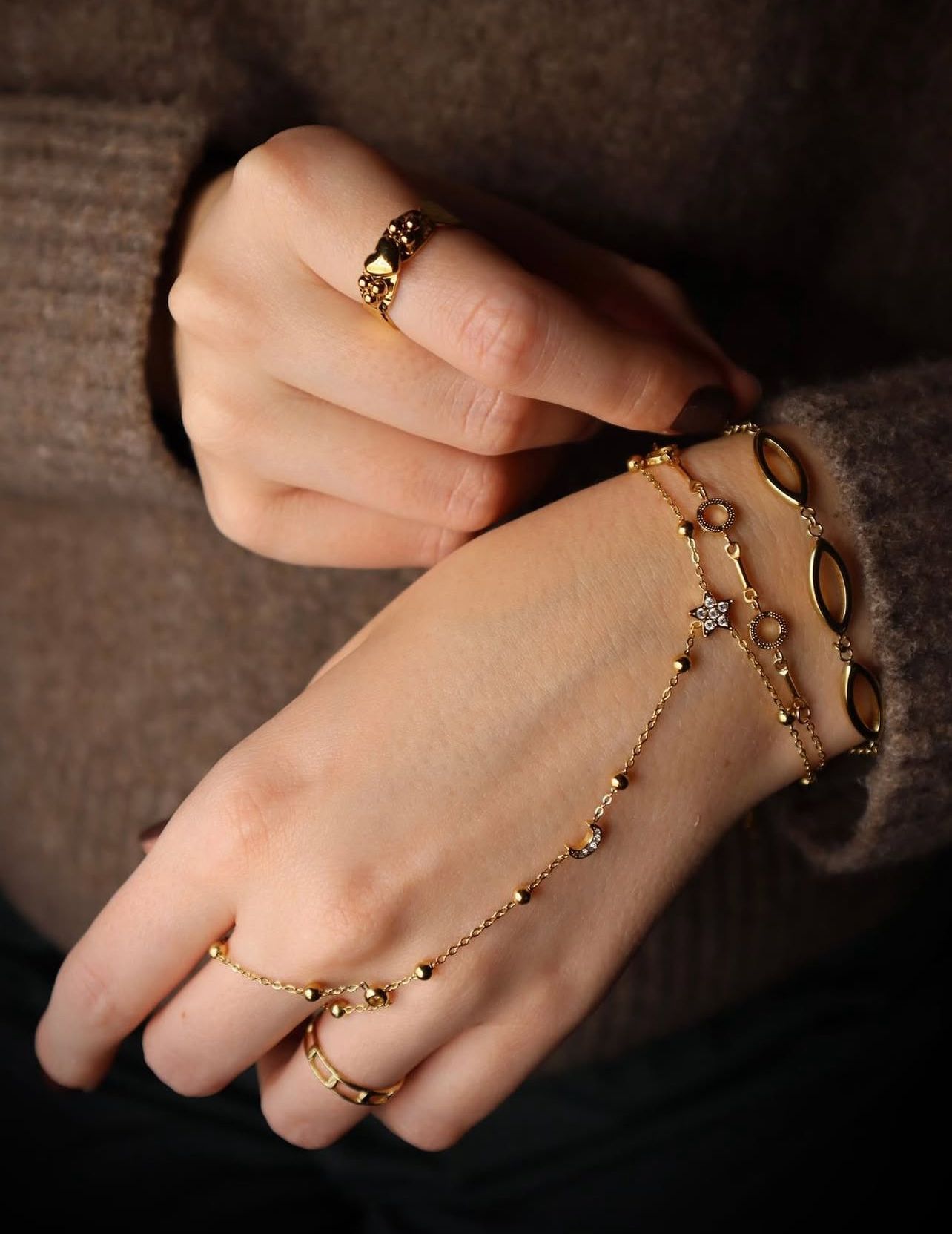 Een persoon draagt gouden ringen en een ingewikkelde, armband met delicate kralen en een klein, fonkelend steentje.