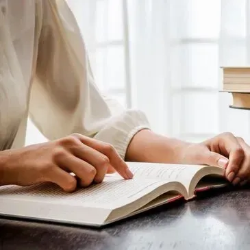 A woman is sitting at a table reading a book.