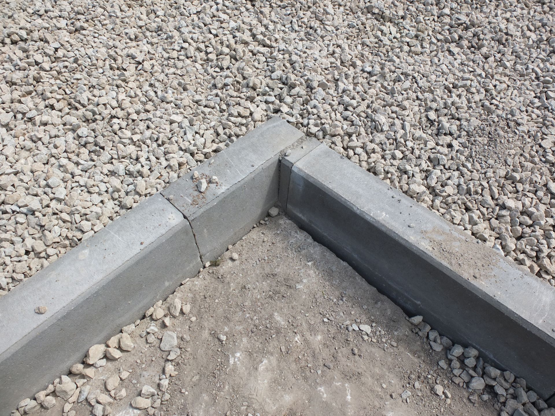 A gravel path winds uphill with yellow wildflowers, and a stone wall on one side.