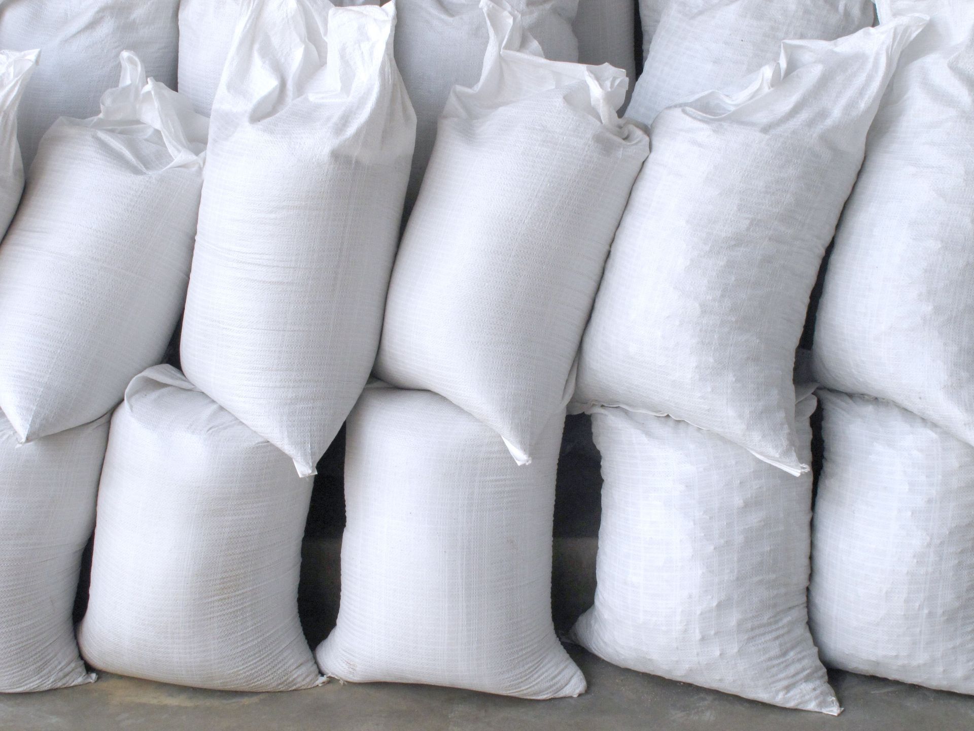 Pile of white, filled sacks, possibly holding grain or other bulk material.