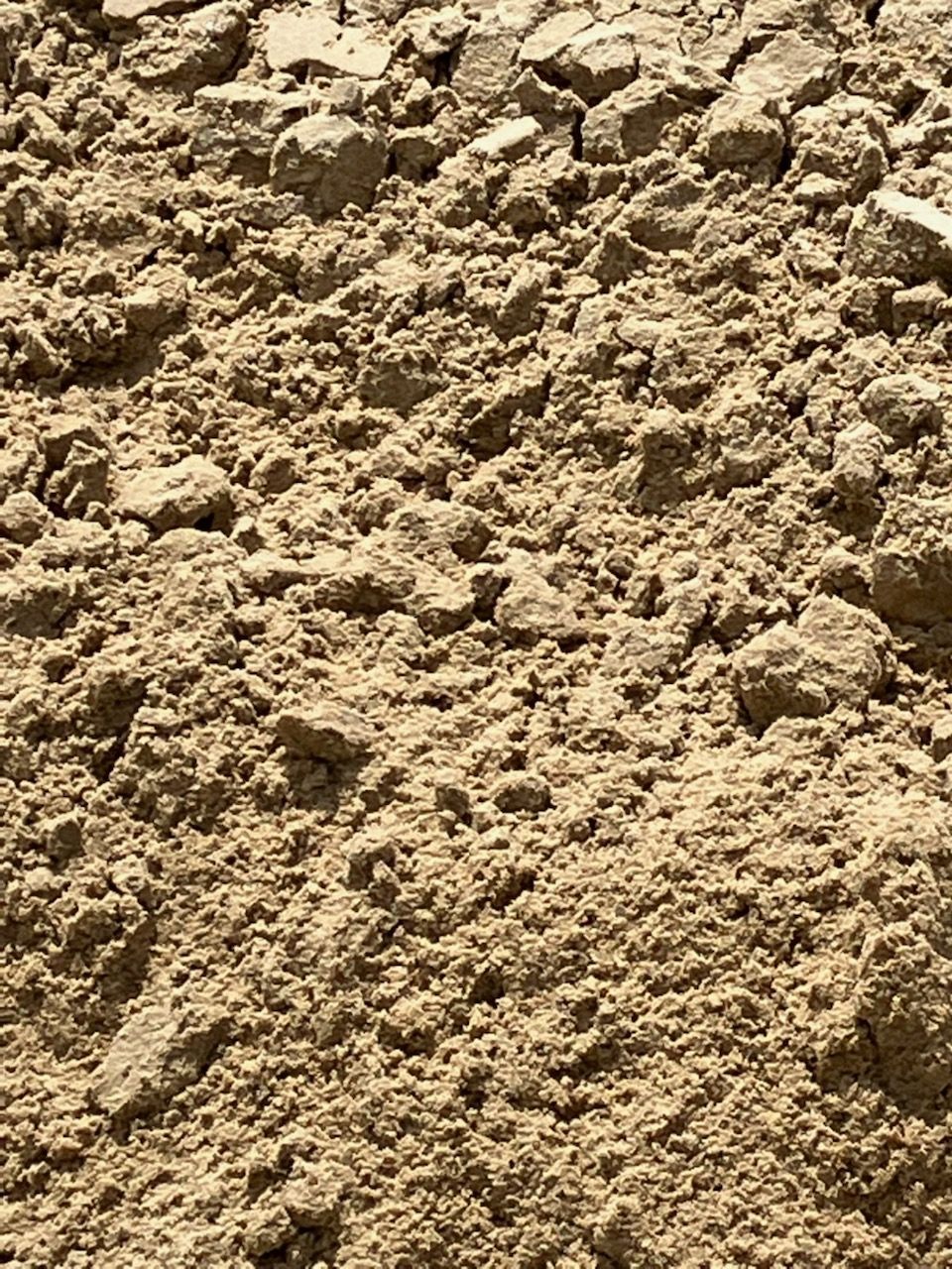 Pile of brown dirt with a white house in the blurred background under a blue sky.