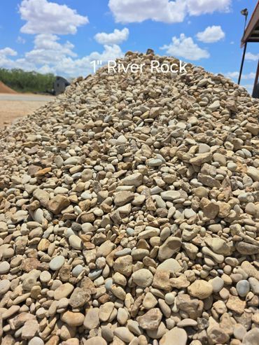 Pile of 1-inch river rocks, mostly tan and gray, under a blue sky with clouds.