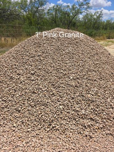 Pile of 1-inch pink granite gravel with a background of trees and a bright sky.