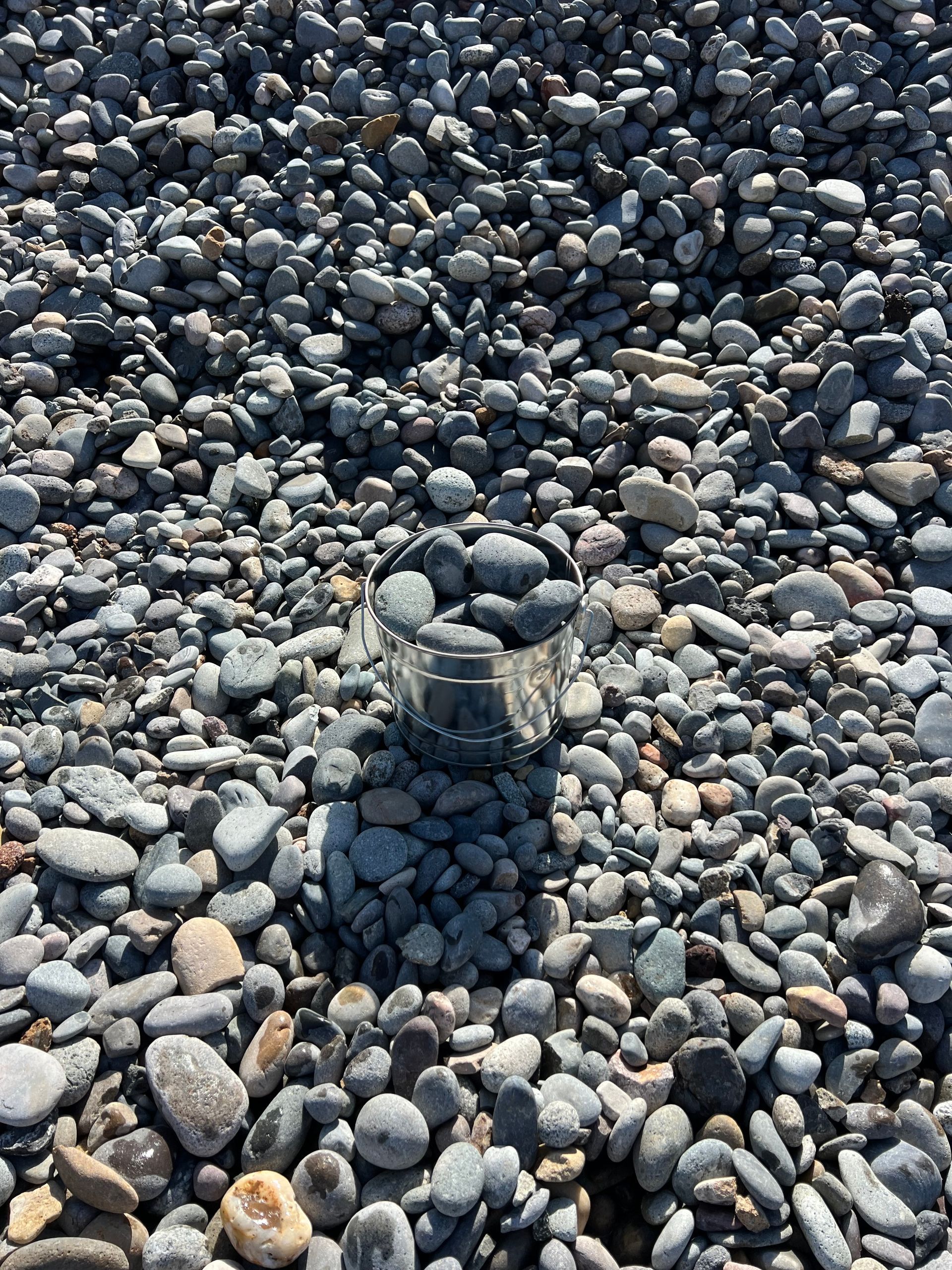 A black bucket filled with rocks is sitting on top of a pile of rocks.