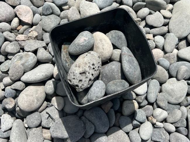 A black container filled with rocks is sitting on top of a pile of rocks.