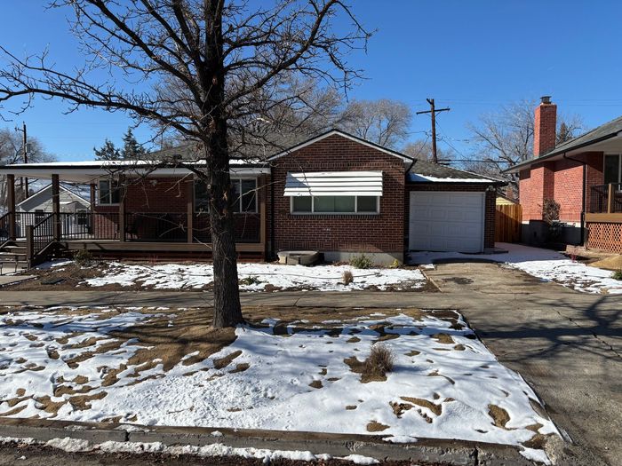 A house with snow on the ground and a tree in front of it.