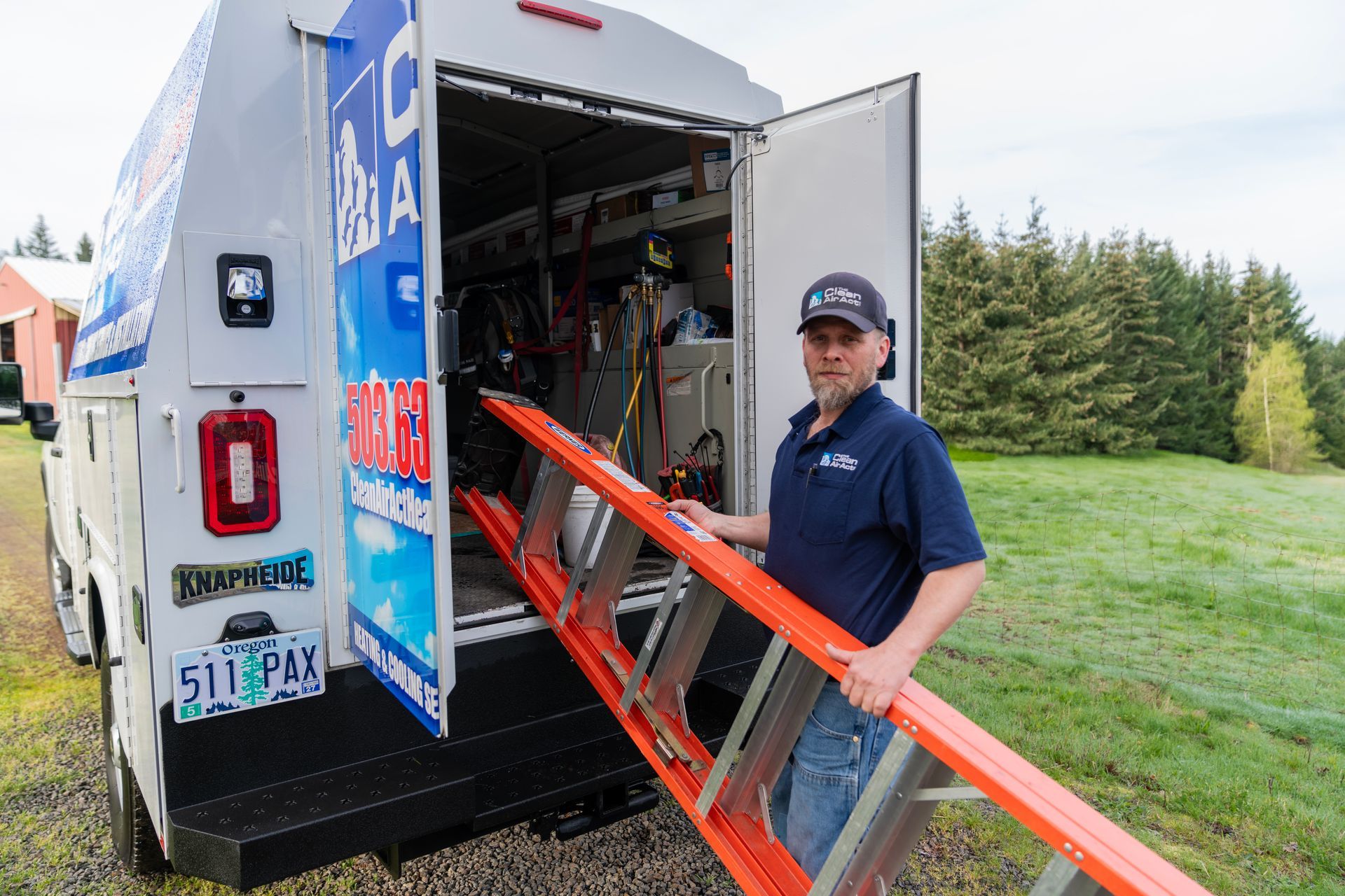 The Clean Air Act Technician is holding an orange ladder in front of a truck.