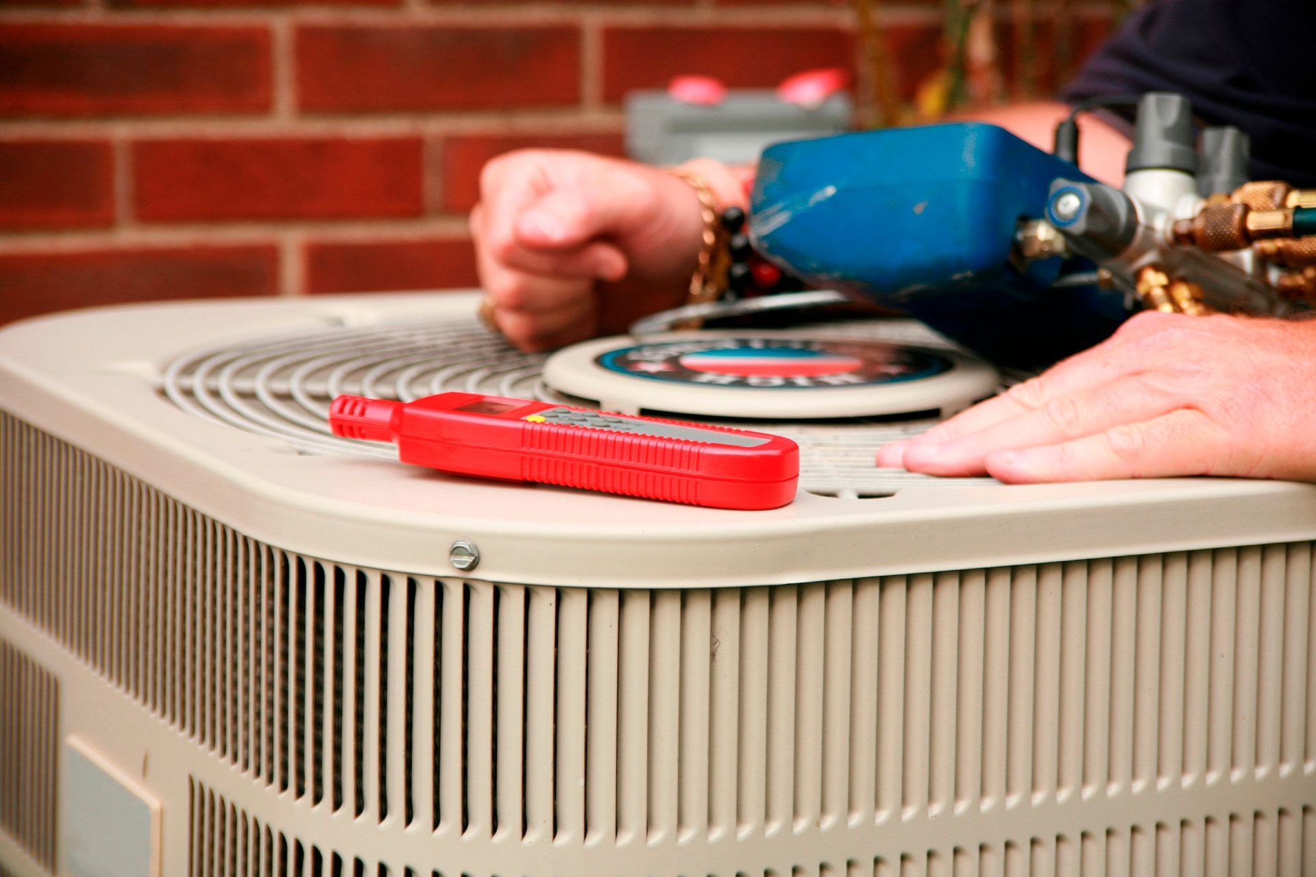 A man is working on an air conditioner outside of a brick building.