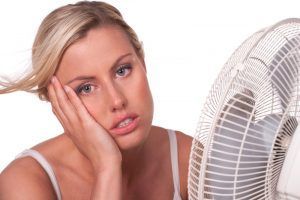 A woman is sitting in front of a fan with her hand on her face.