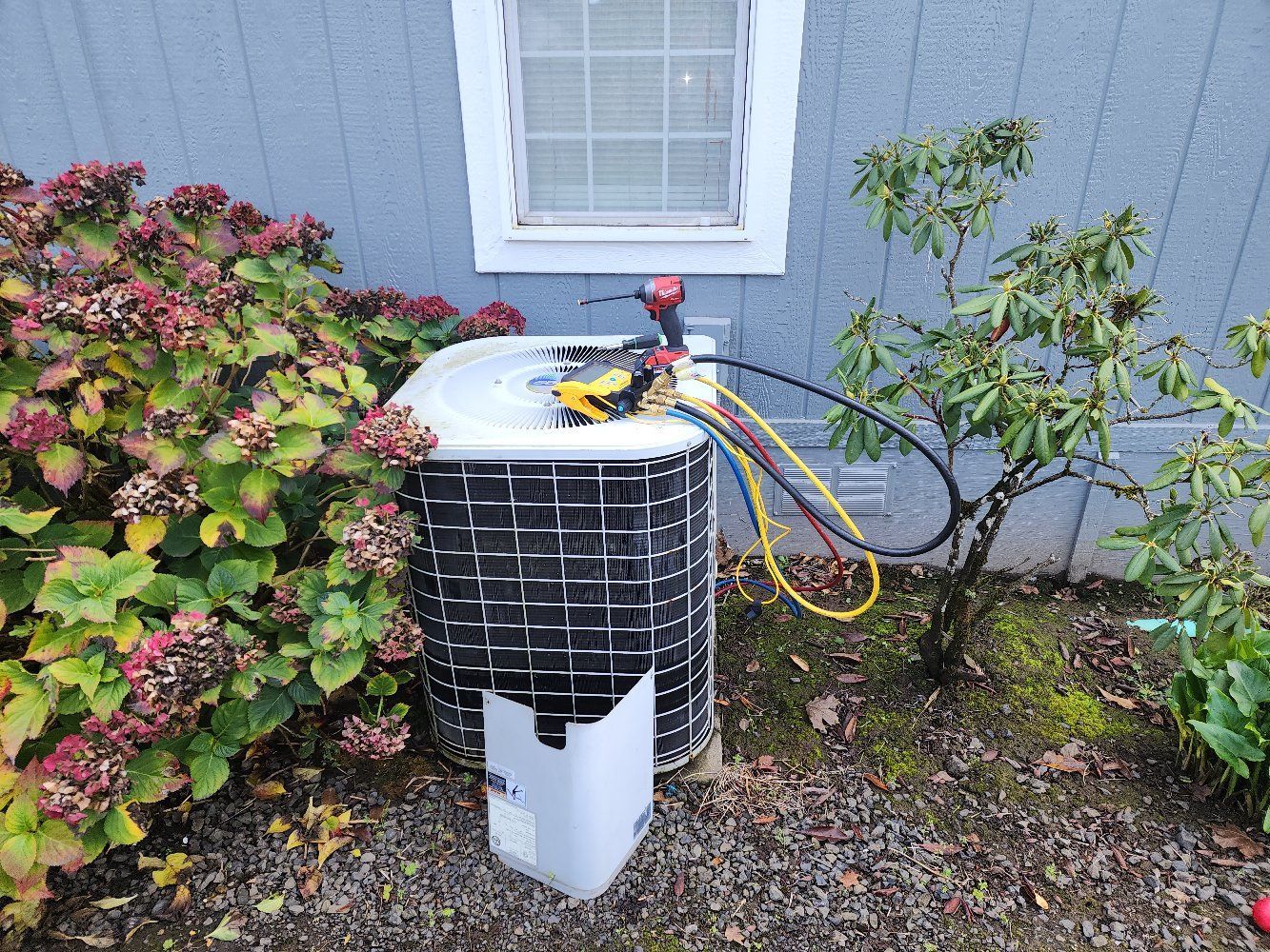 An air conditioner is sitting outside of a house next to a window.