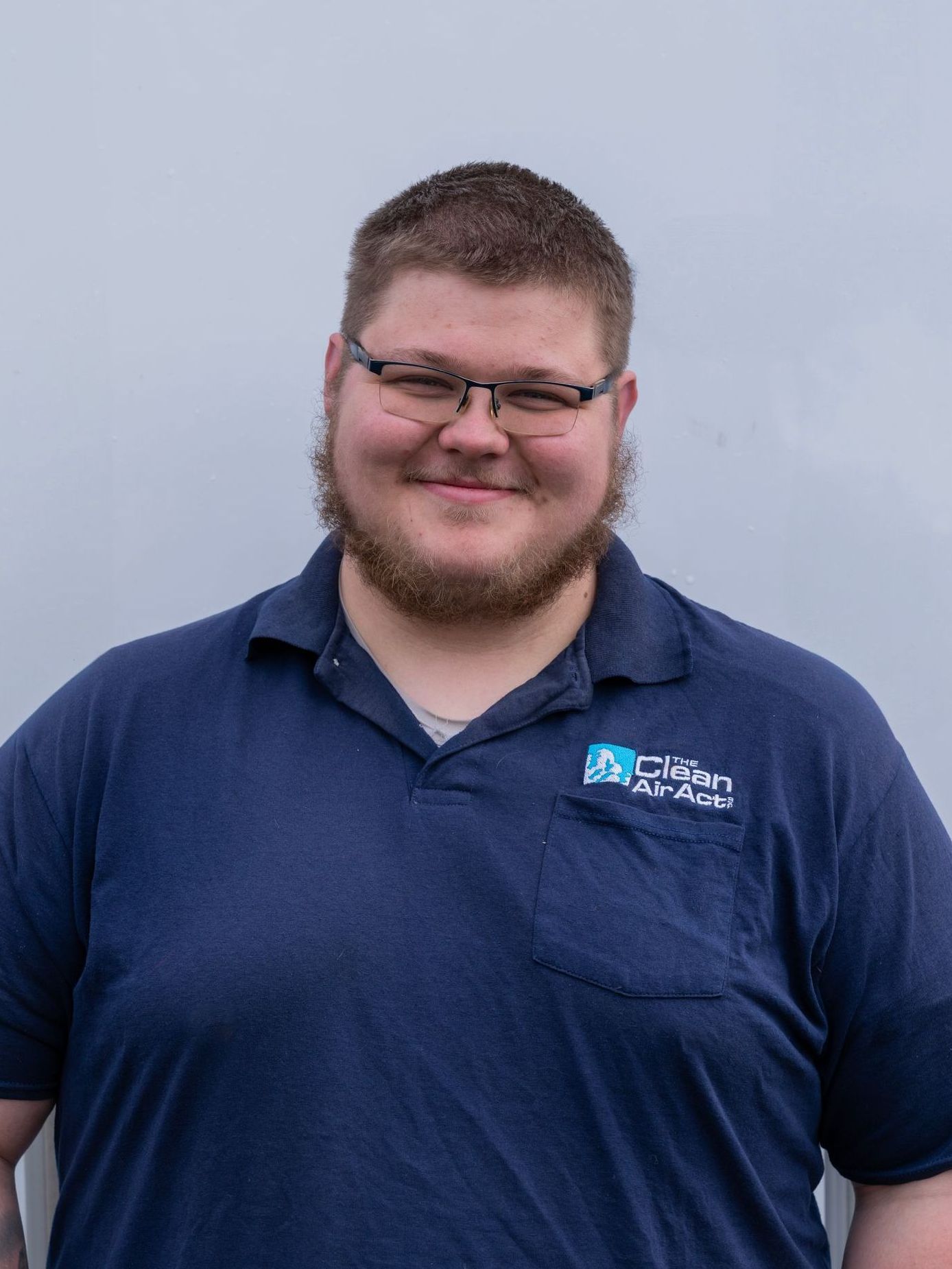 A man with a beard and glasses is wearing a blue shirt and smiling.