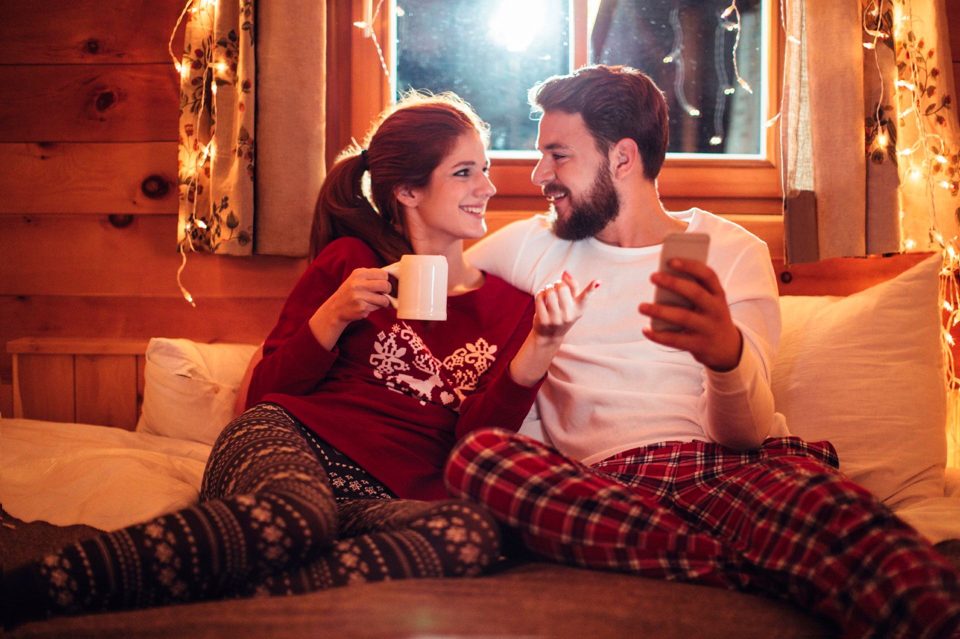 A man and a woman are sitting on a bed looking at a cell phone.