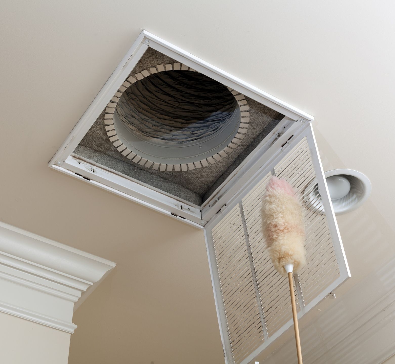 A person is cleaning a ceiling vent with a duster.