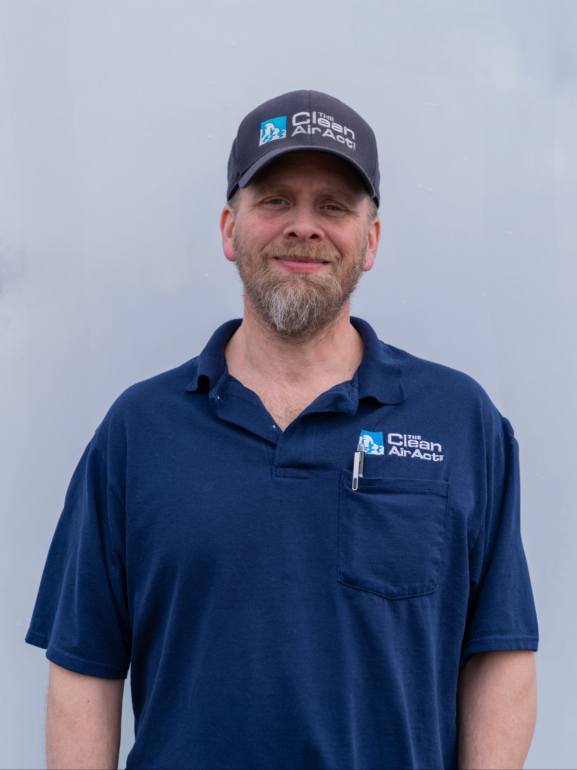 A man wearing a hat and a blue shirt is standing in front of a wall.