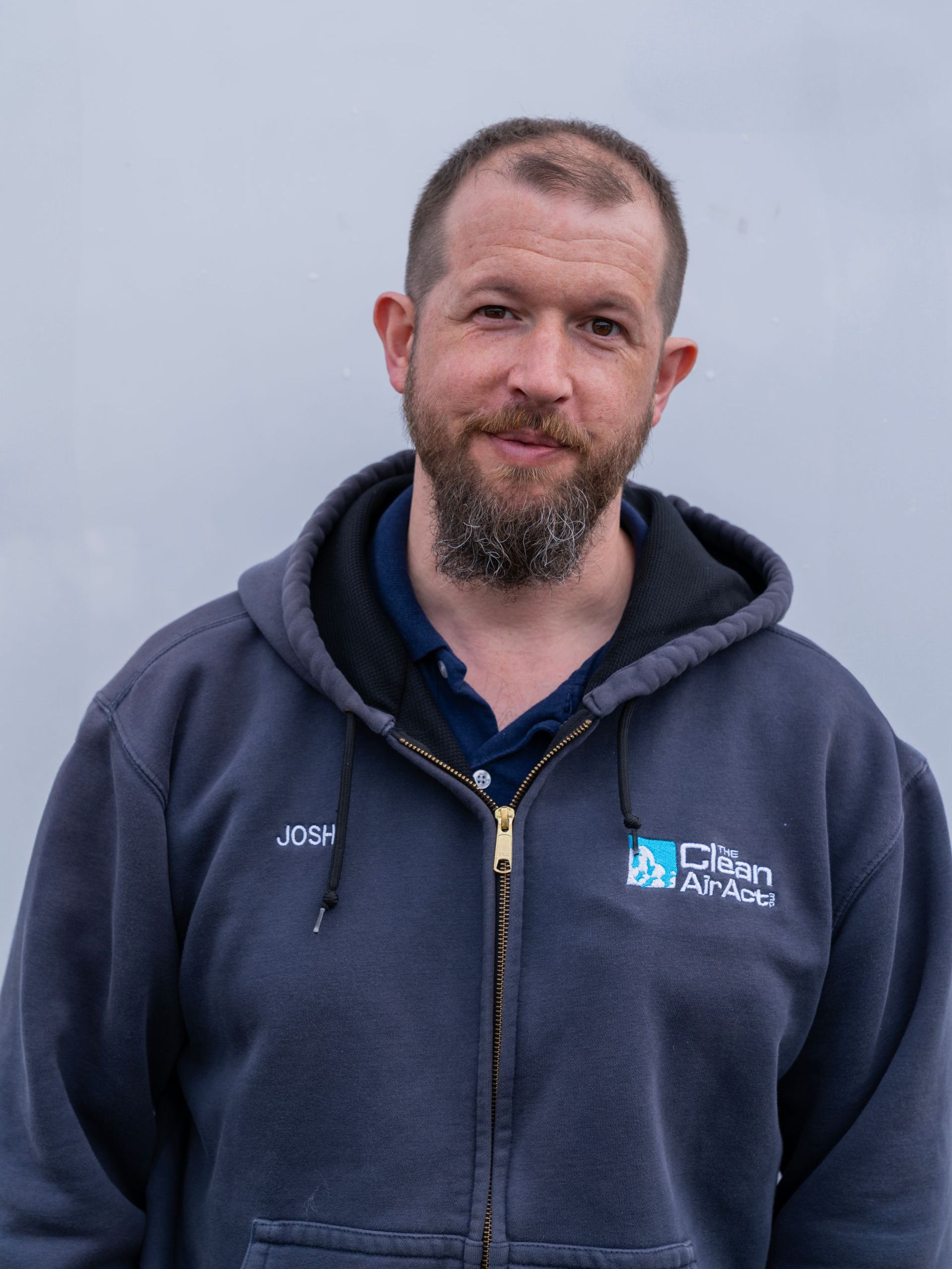A man with a beard is wearing a hoodie and a blue shirt.