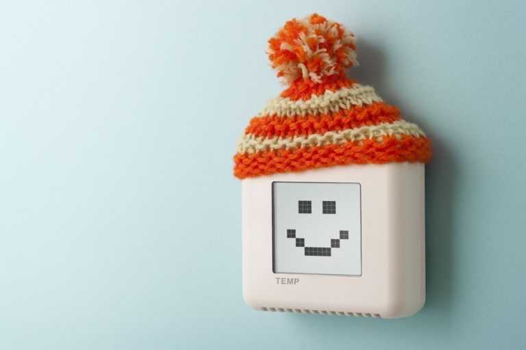 A thermostat with a smiley face on it is covered in a knitted hat.