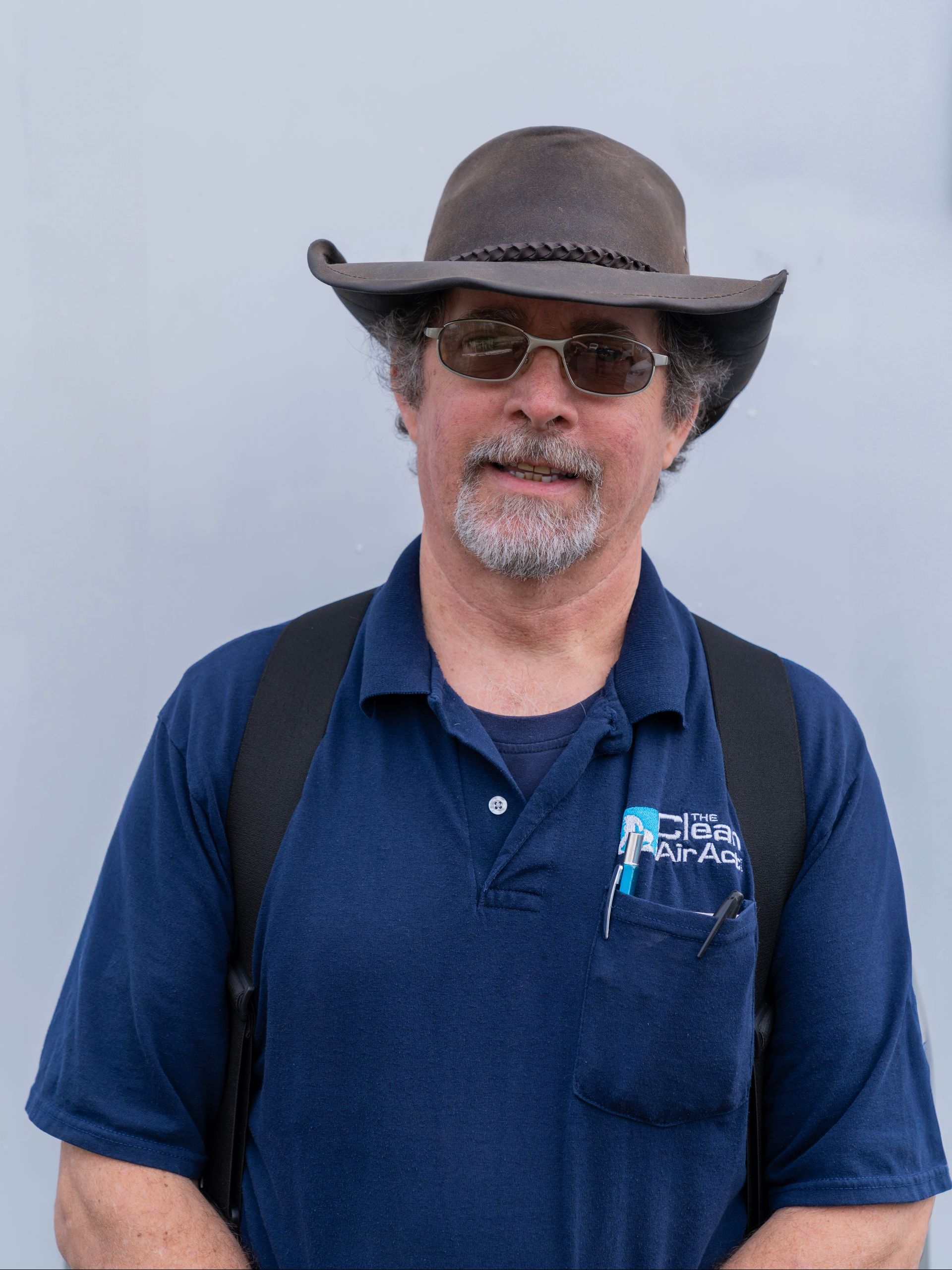 A man wearing a hat and sunglasses is standing in front of a white wall.