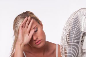 A woman is holding her head in front of a fan.