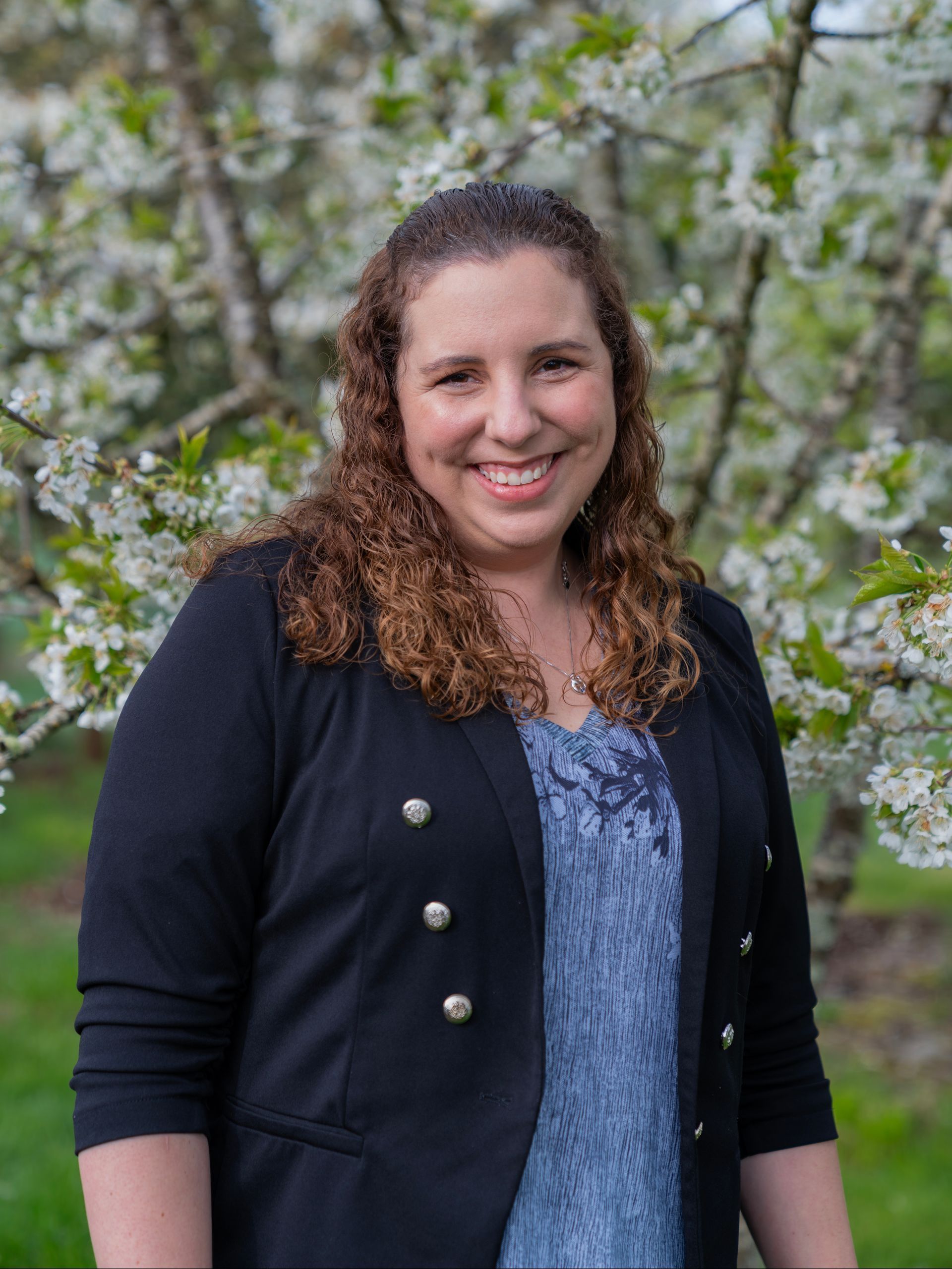 A woman is standing in front of a tree with white flowers.