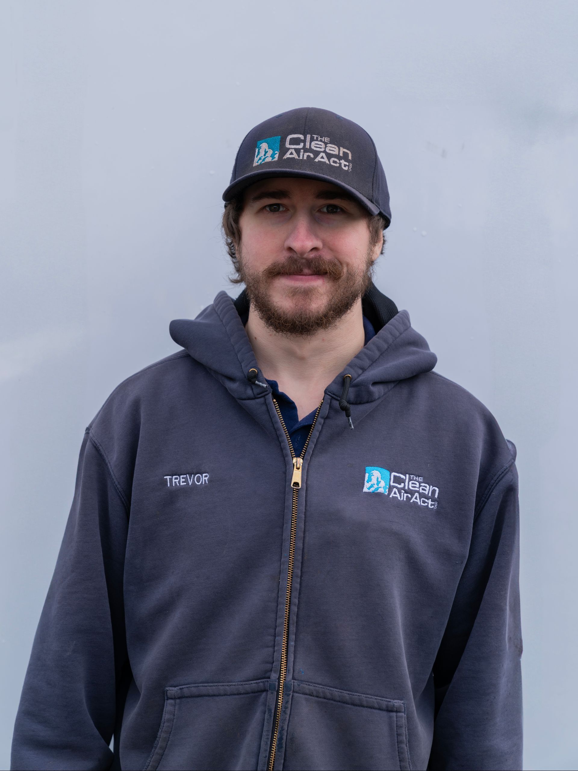 A man wearing a hat and a hoodie is standing in front of a white background.