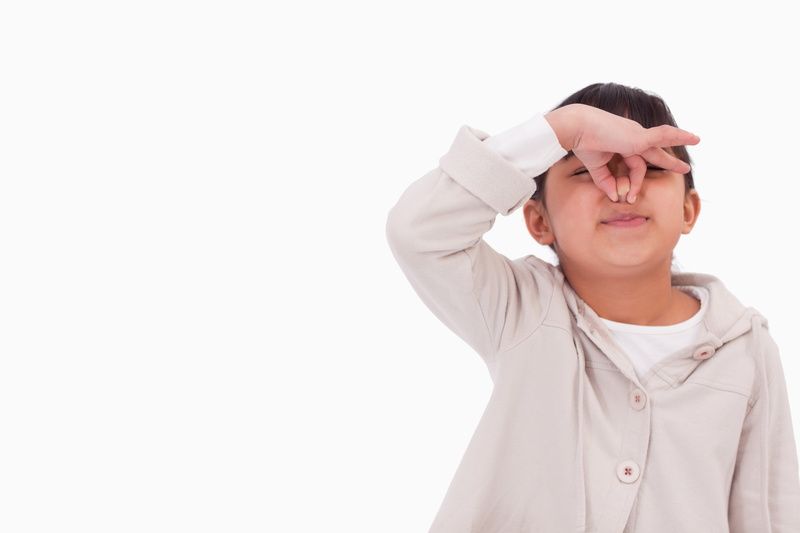 A young boy is covering his nose with his hand.