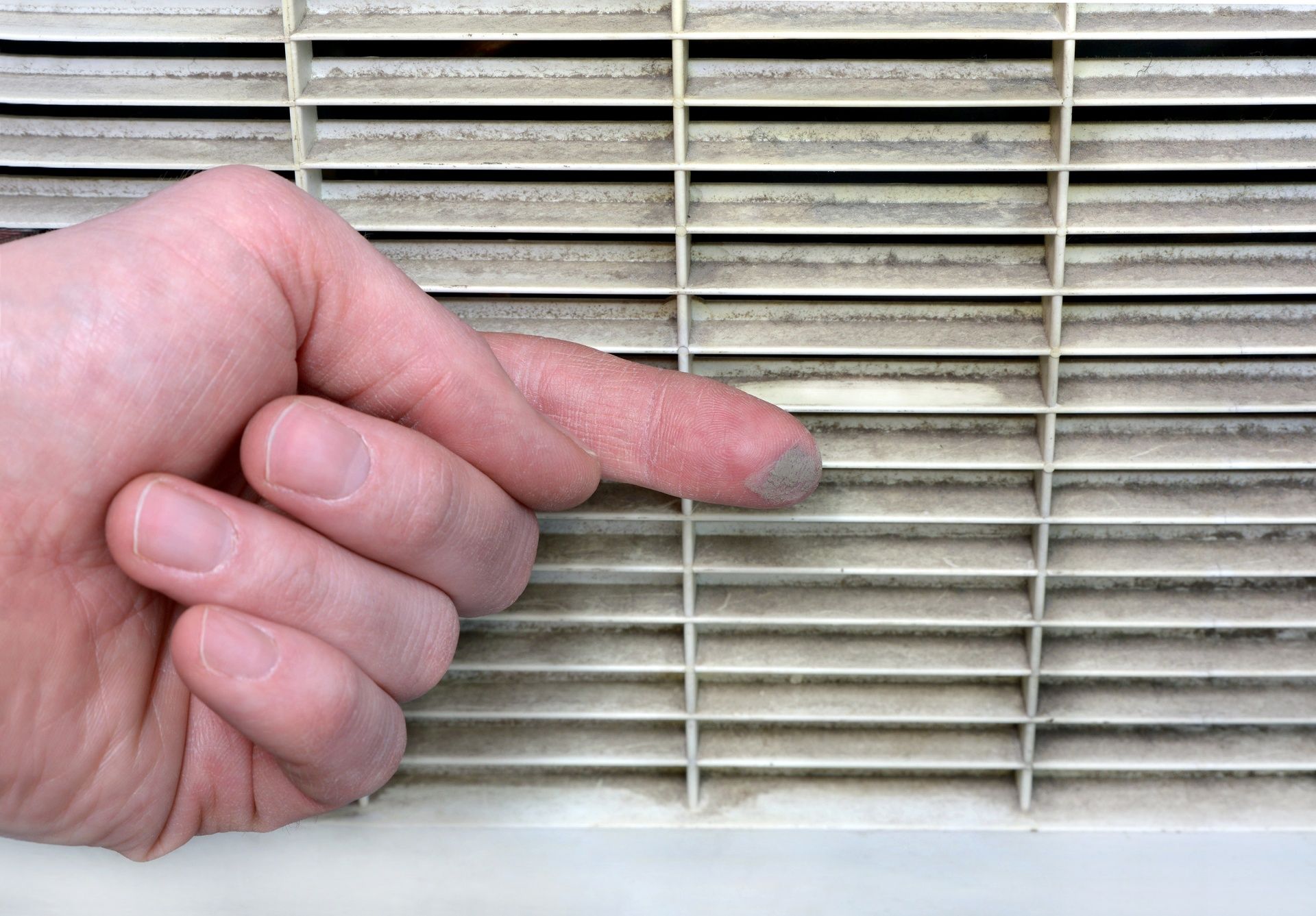 A person is pointing at a dirty air vent with their finger.