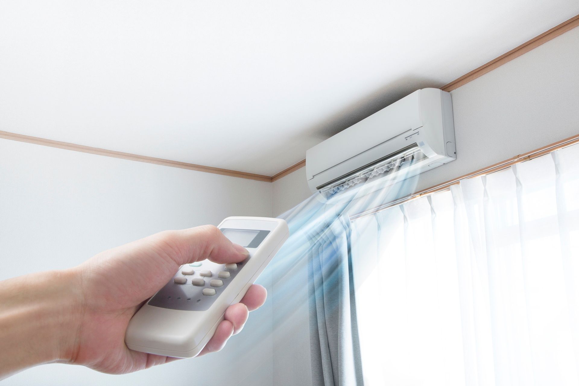 A person is holding a remote control in front of an air conditioner.