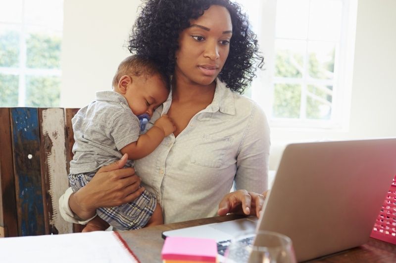 A woman is holding a baby while using a laptop computer.