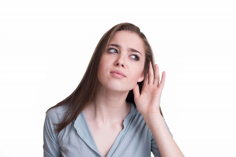 A woman is listening to something with her hand to her ear.