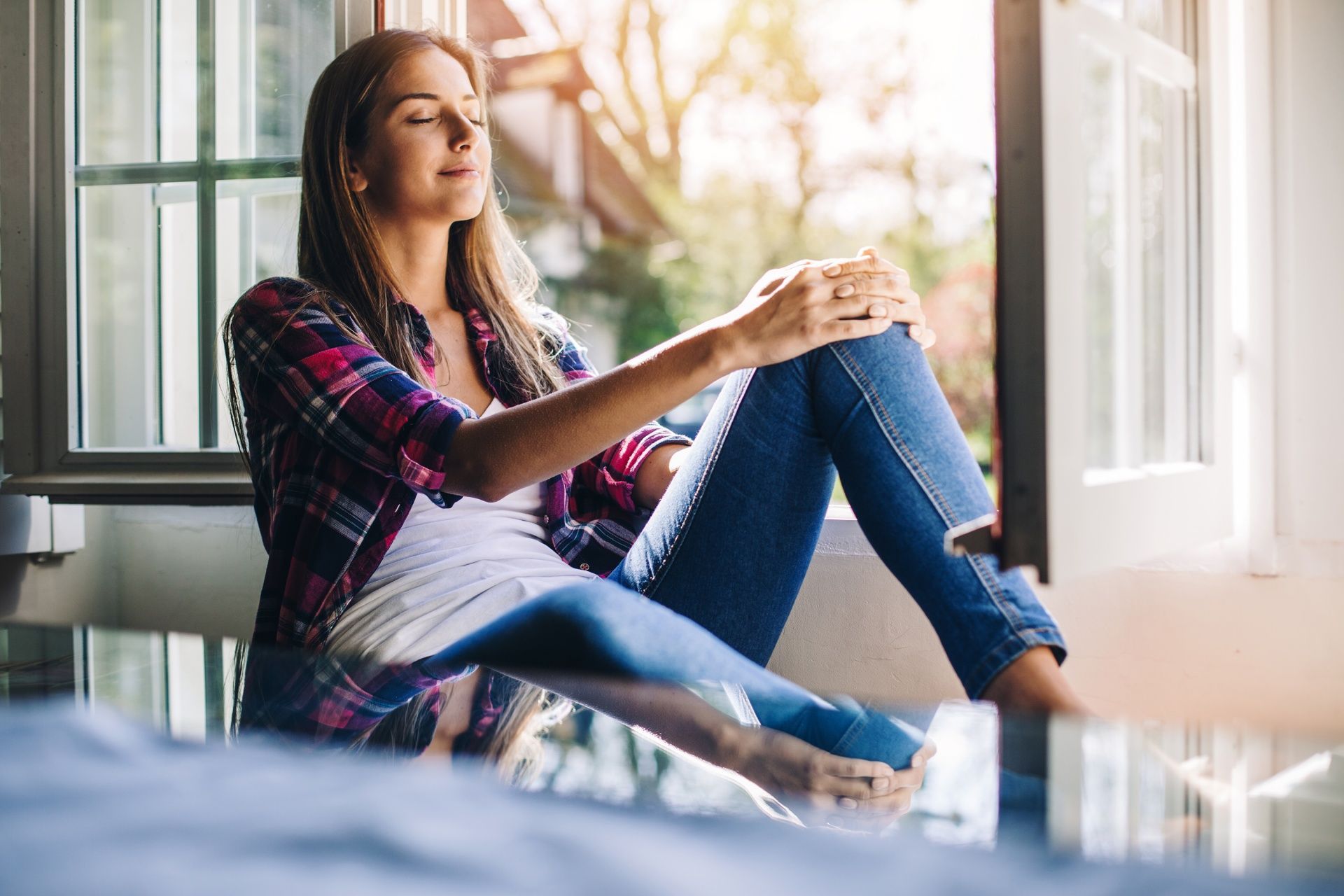 A woman is sitting on a window sill looking out the window.