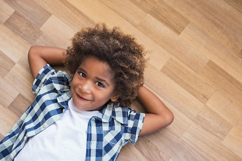 A young boy is laying on a wooden floor with his hands behind his head and smiling.