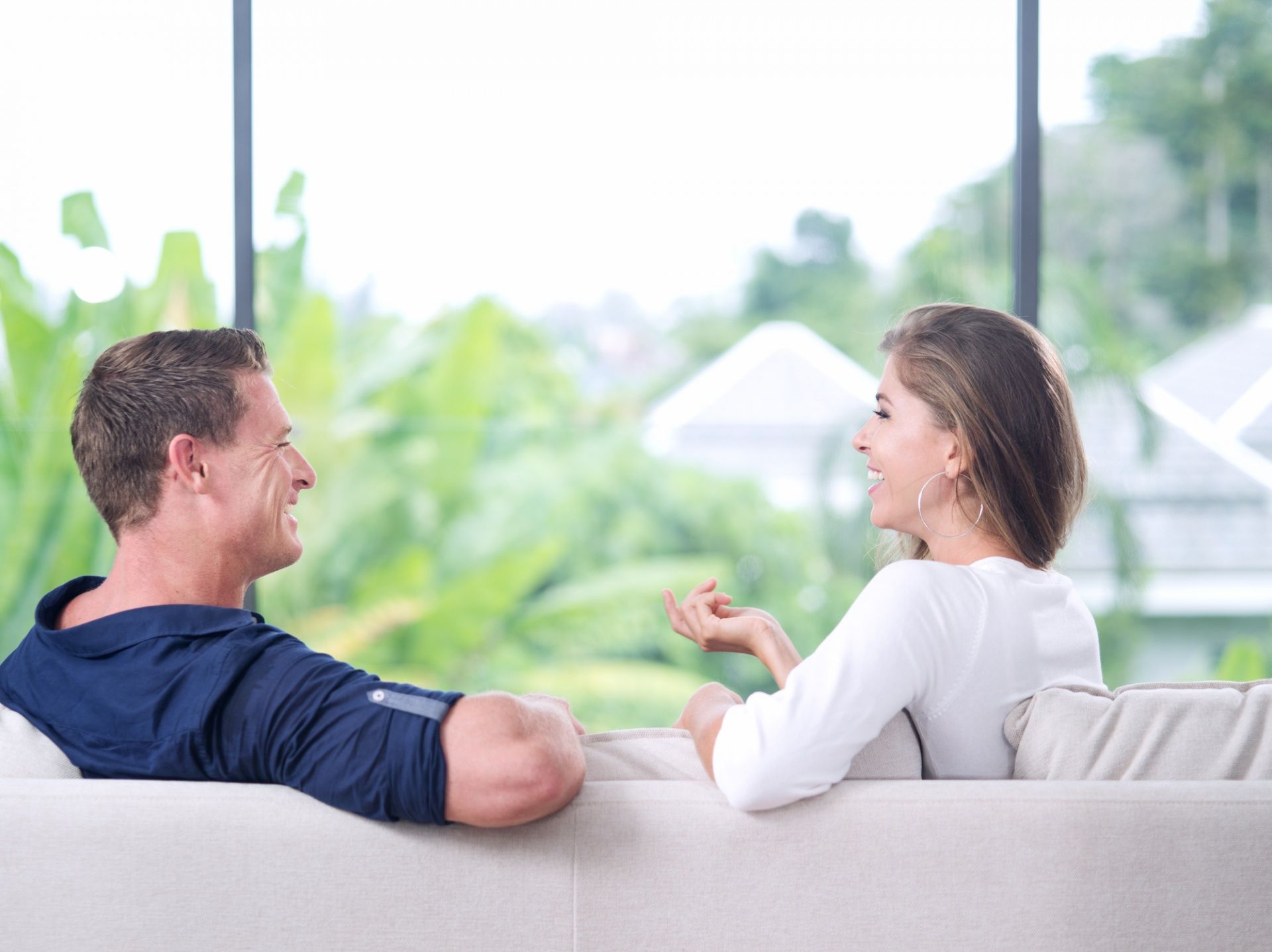 A man and a woman are sitting on a couch talking to each other.