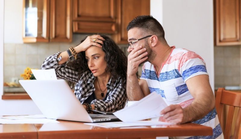 A man and a woman are sitting at a table looking at papers and a laptop.