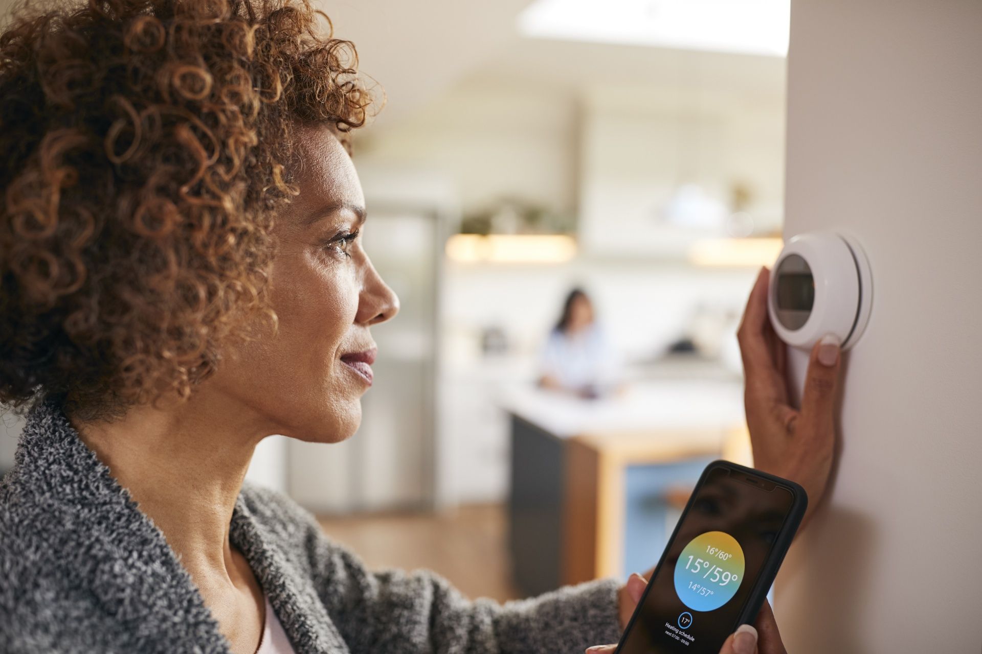 A woman is adjusting her thermostat with a smart phone.
